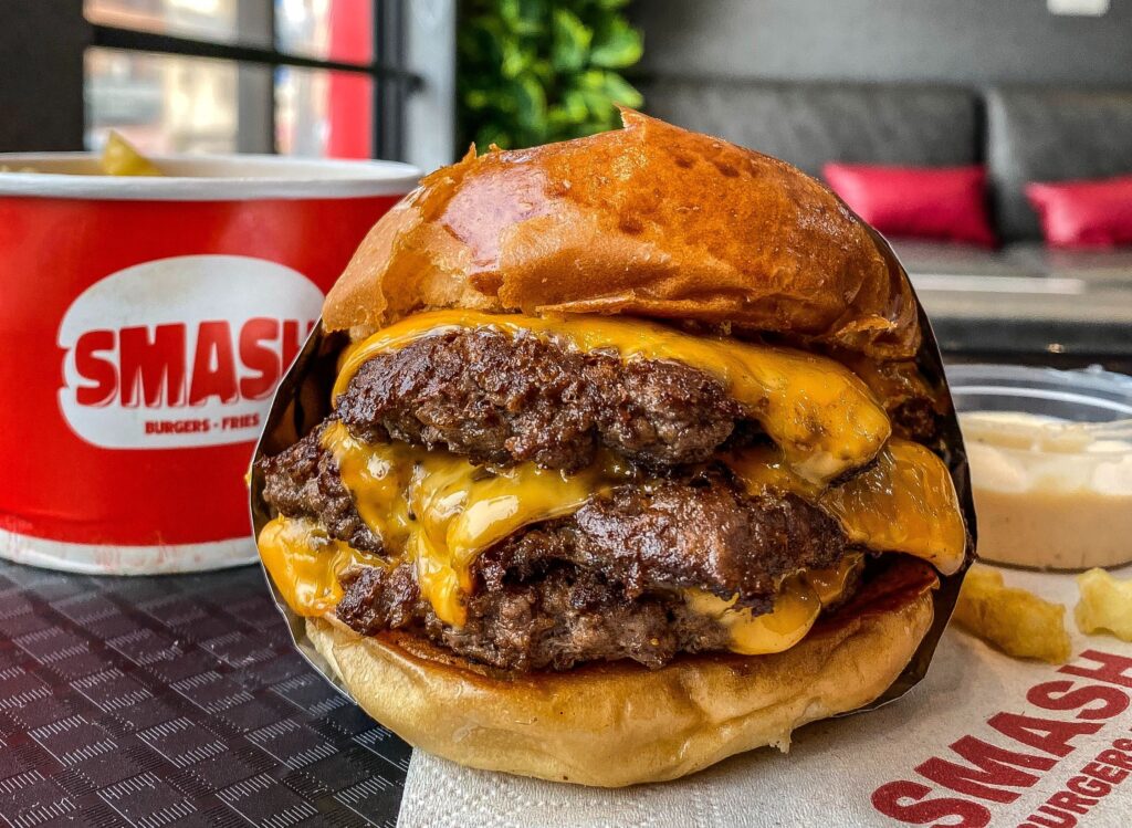 A cheeseburger with melted cheese and a cup of fries on a table.