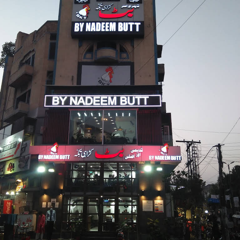 A large building with a sign that reads "By Nadeem Butt" stands tall.