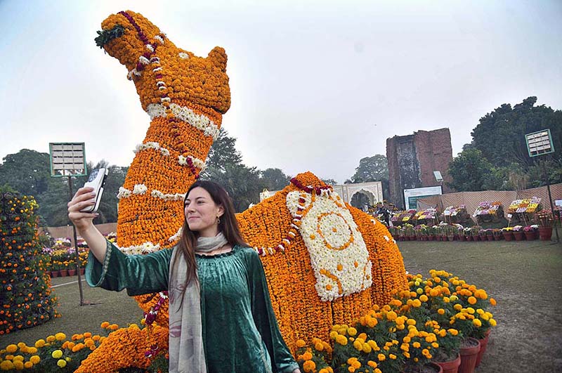 A woman capturing a selfie with a floral camel sculpture. A unique blend of nature and artistry.