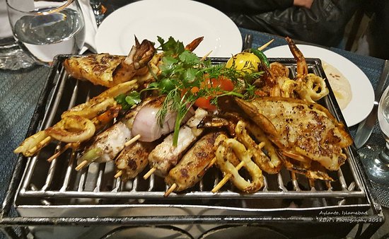 A grill with assorted food cooking on it, placed on a table outdoors.